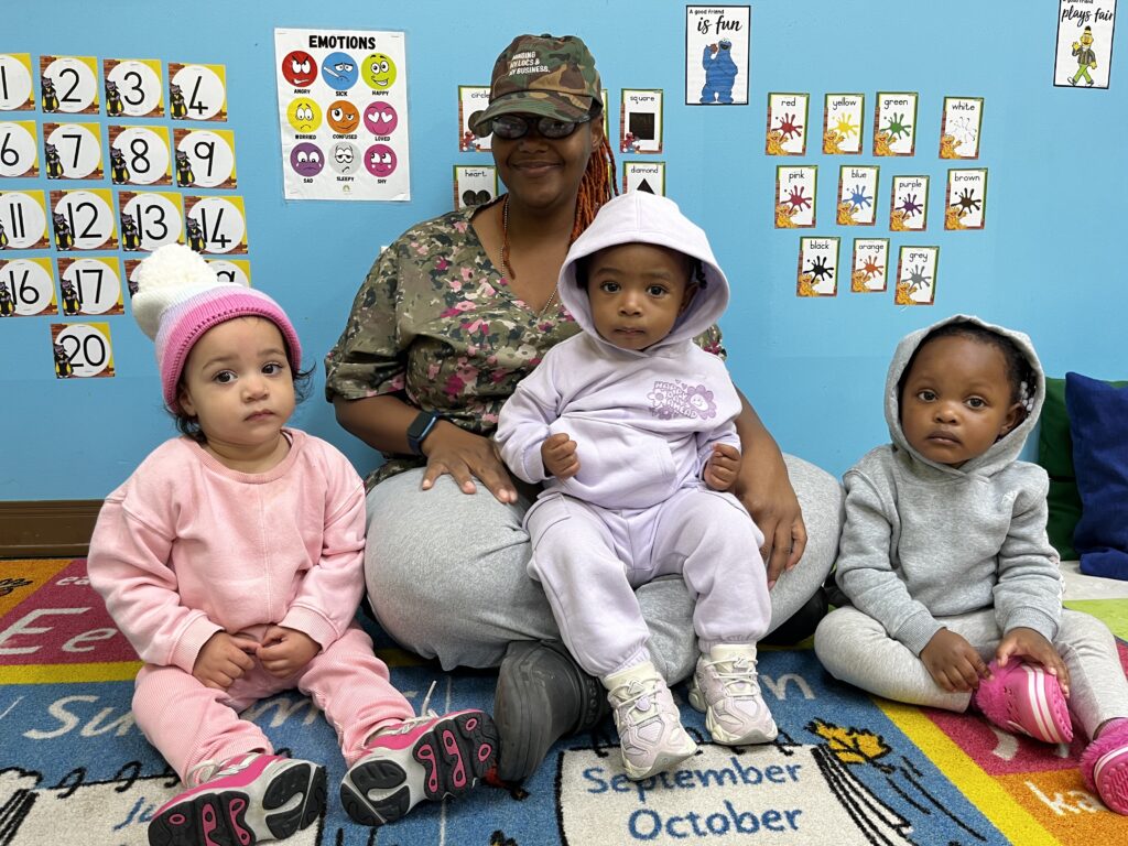 Toddler 1 students sitting on the carpet with their teacher.